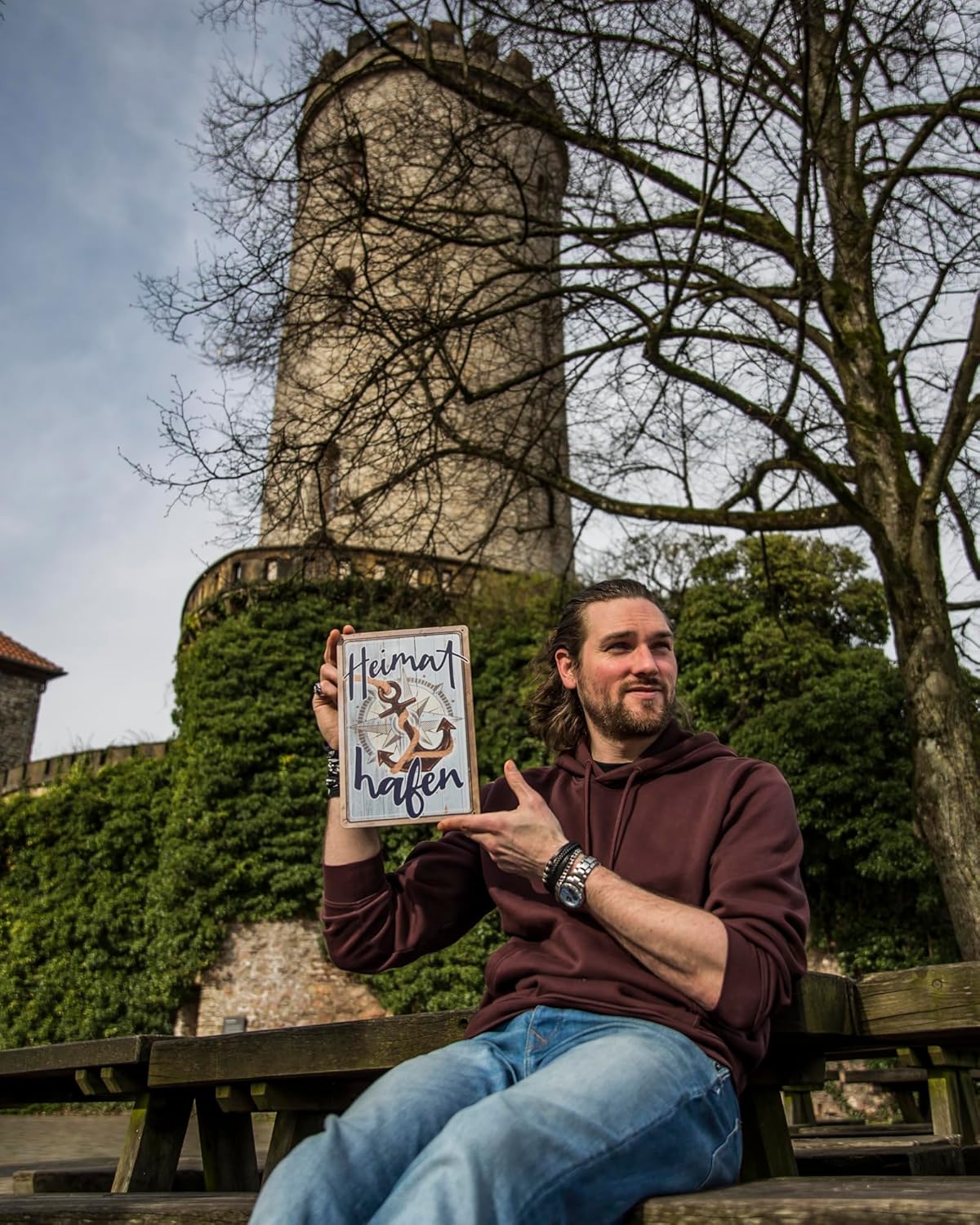 Mann sitzt auf einer Bank vor der Sparrenburg und hält Blechschild mit Aufschrift Heimathafen hoch