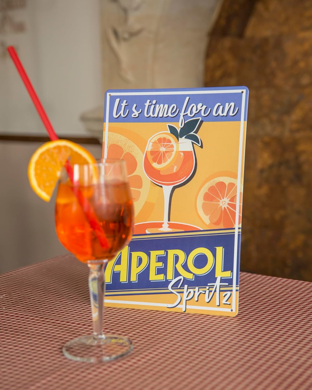 Blechschild mit Aufschrift It's time for an Aperol Spritz neben Aperol Spritz Glas