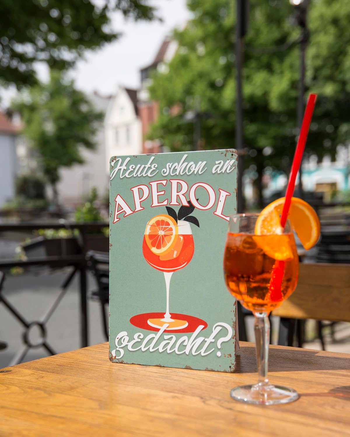 Blechschild mit Aperol-Motiv auf einem Tisch mit Aperol Spritz-Glas